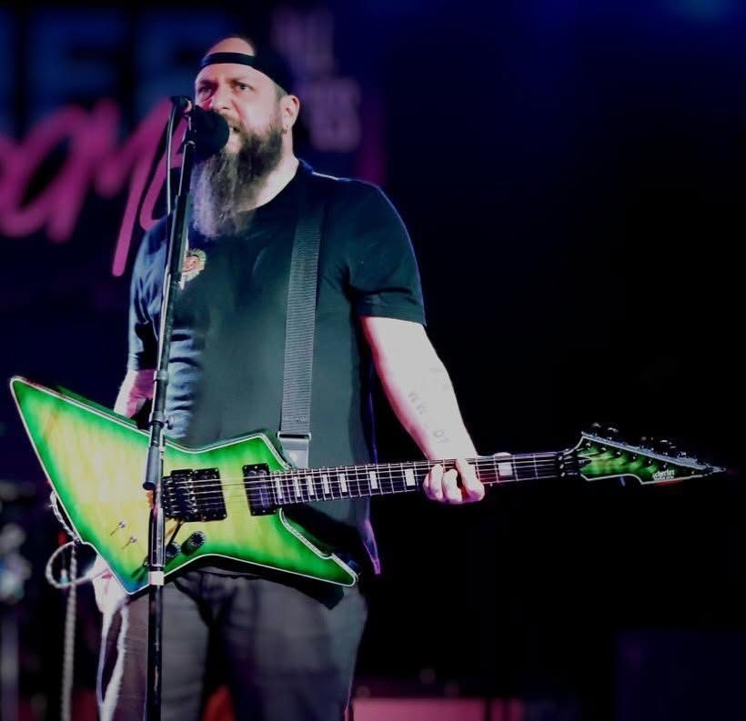 Nate Laff singing with a green Schecter Explorer-style guitar under blue light