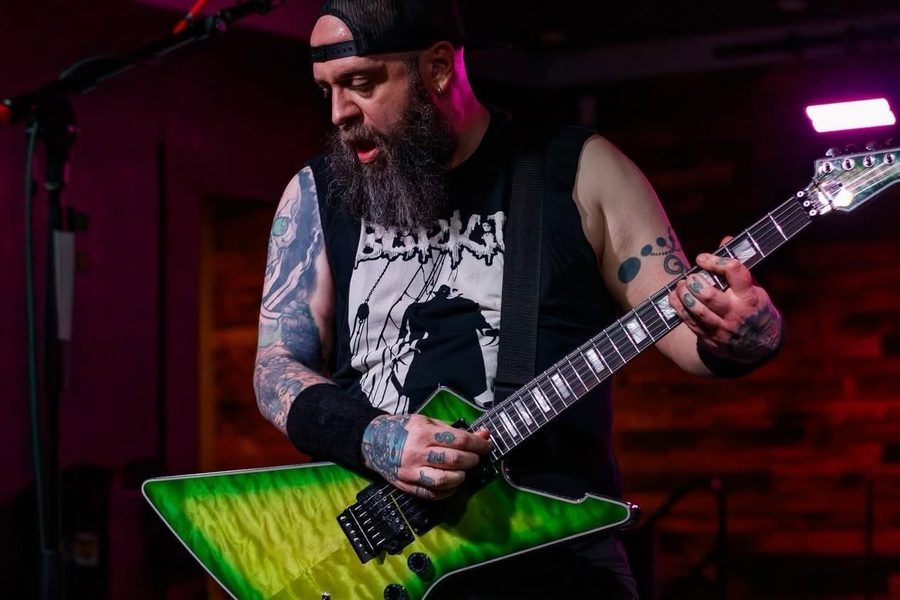 Nate Laff playing a green Schecter Explorer-style guitar on stage